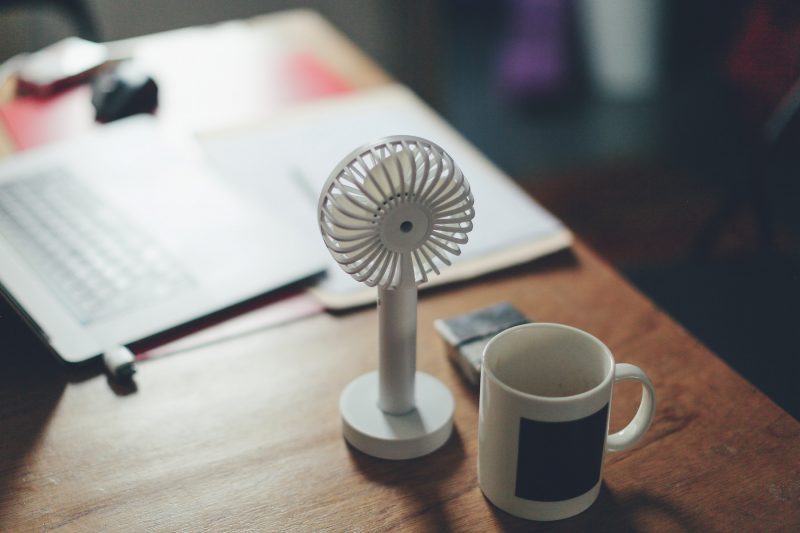 Photo of a personal fan sitting on a work desk next to a cup of coffee